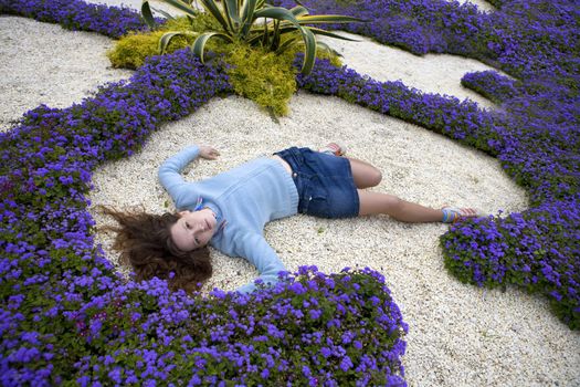 Attractive young serious woman lying between blue flower on white stone