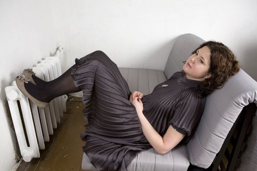 Portrait of young adorable pensive  woman wearing grey dress sitting on sofa put her legs on radiator