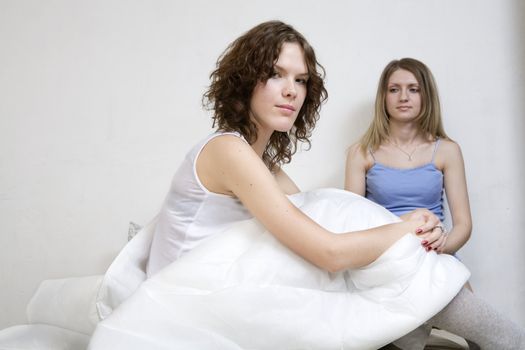 attractive thoughtful blond  woman with a pillow on the bed. Her friend sitting near her.  Women`s friendship