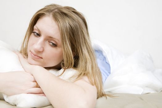 attractive thoughtful blond woman hugging  pillow on the bed. Woman`s problem