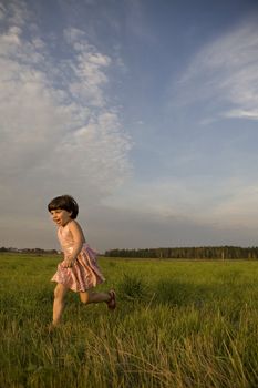 little cute girl running on meadow in sunset time. Summer time