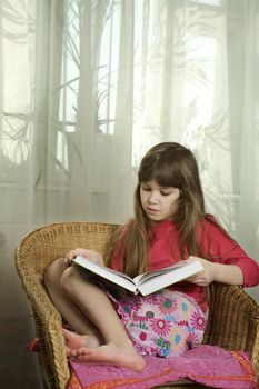 little cute serious girl reading book sitting in chair