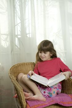 little cute serious girl seven years old reading book sitting in chair