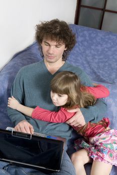 Father and daughter playing game sitting on the sofa using a laptop computer
