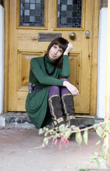 portrait young attractive  woman sitting on doorstep at door wearing green dress and violet stocking