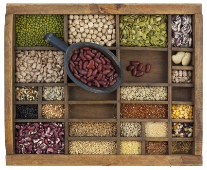 rustic scoop of red kidney beans and a variety of lentils, grain, seeds in old wooden typesetter case, isolated with clipping path