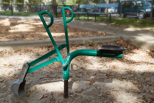 Green metal childrens playground shovel with soft focus bench and fence in background