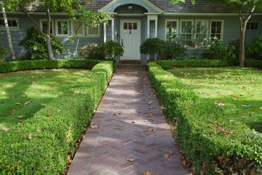 Green bush lined home brick entrance to a white doored gray home