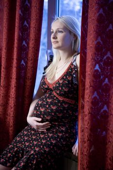 attractive pregnant blond  serious woman at window