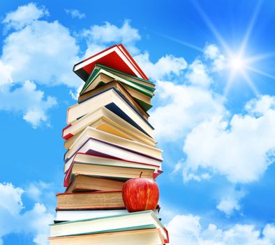Pile of books and apple against blue sky with clouds