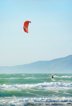 Surfer with red kite surfing off the beach in San Francisco, California on a sunny day.