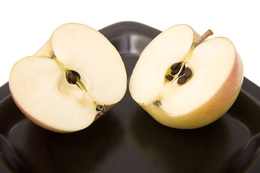 Two halves of an apple on a black plate on a white background