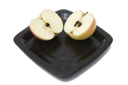 Two halves of an apple on a black plate on a white background