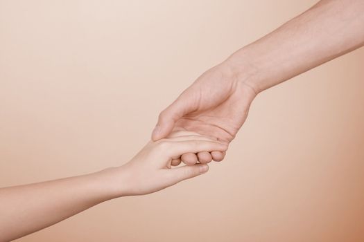 The man's hand holds a hand of the child on a beige background