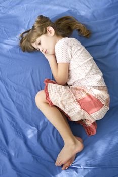 little dreaming girl lying on the bed. Blue cotton sheet