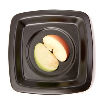 Two halves of an apple on a black plate on a white background