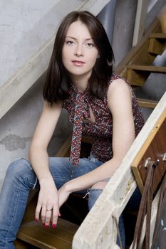 young attractive smiling  girl in jeans having a hole sitting on stairs