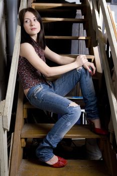 young attractive smiling  girl in jeans having a hole sitting on stairs