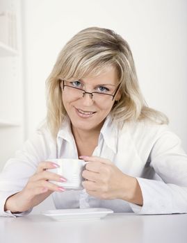 The young happy woman drinks tea or coffee at office