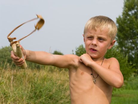 The boy shoots from a wooden slingshot in the afternoon.