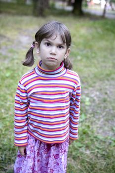 little cute serious six years old girl standing in forest