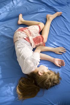 little dreaming girl lying on the bed. Blue cotton sheet