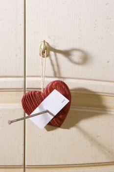 Wooden heart with nail hang on door of white  wardrobe. You can write on white note "yours sincerely"