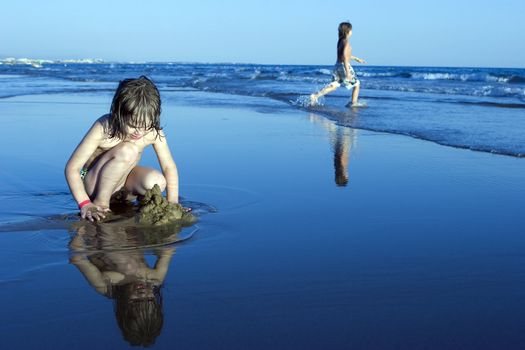 Little cute girl playing in sand on shore in suset