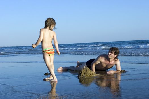 Father and daughter build sand castle on seashore