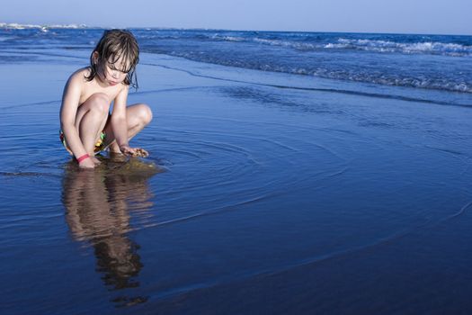 Little cute girl playing in sand on shore in suset
