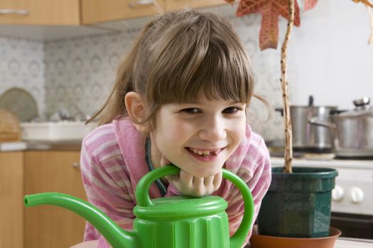 little cute girl seven years old with watering-can sitting on kitchen

