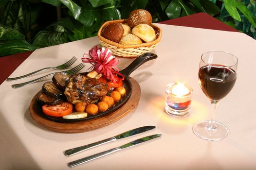 Fried meat on a table, wine, a candle and a roll