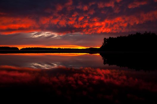 Beautiful mirror image showcasing natures natural colors at sunset in Tofino, B.C., Canada, a popular surf destination on Vancouver Islands Pacific Rim.  Silhouette of treeline & distant island cut the image in half.