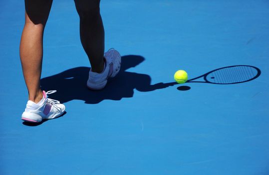 A female tennis players legs are shown with the shadow of the raquet and ball.