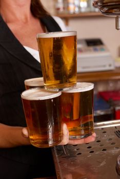 Skilful waitress balancing four full beer glasses