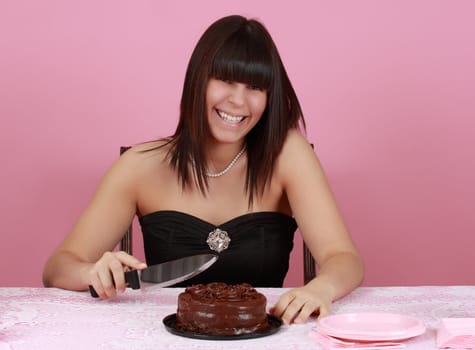 cute girl holding a knife ready to cut a chocolate cake, pink background