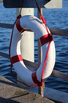 White and red buoy hanging on a metallic fence near the water lake