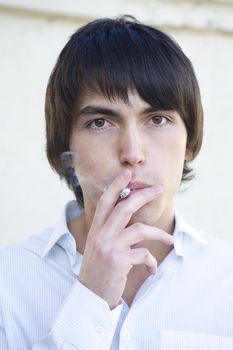 close up portrait of young serious handsome smoking man to exhale smoke.