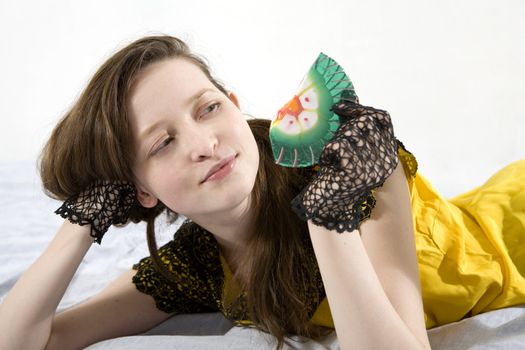 young smiling attractive woman with long hair in yellow dress with green lollipop lying on bed