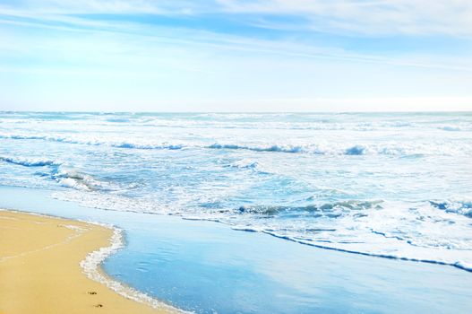 Beach in San Francisco California with waves coming to the sand and blue sky background.