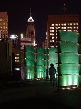 An individual looks at a monument with a cityscape in the background at night.