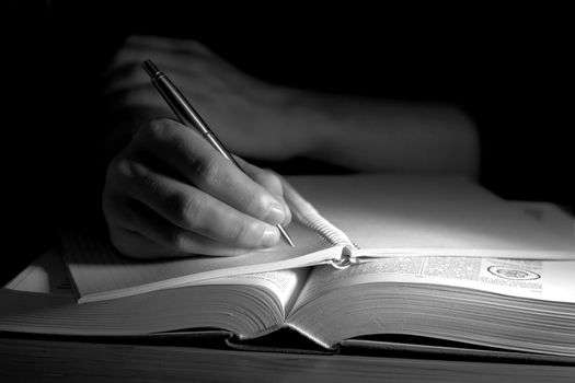 Open book in a dark room, with human hand taking notes