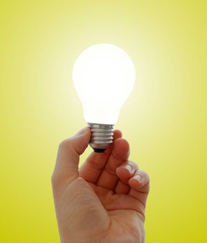 Glowing lightbulb in a hand on yellow background