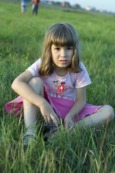 little cute girl sitting in middle of meadow. Summer time. 