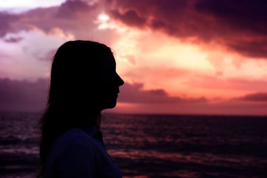 Woman silhouette on the beach looking to the sunset