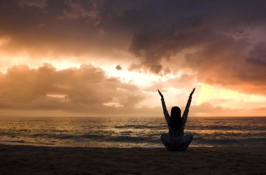 Woman silhouette relaxing on the beach at the sunset