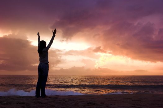 Woman silhouette relaxing on the beach at the sunset