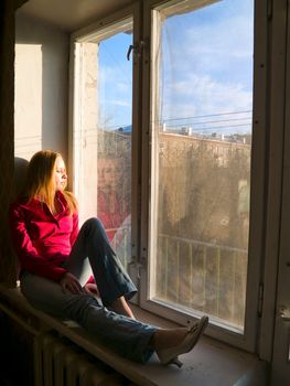 Beauty red-hair girl sitting on window. Thinking and may be dreaming