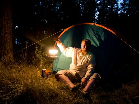 Friendly adult man near his camp play with lantern at night