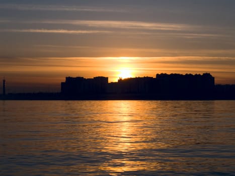 Sunset on a city thought bay with buildings silhouettes
